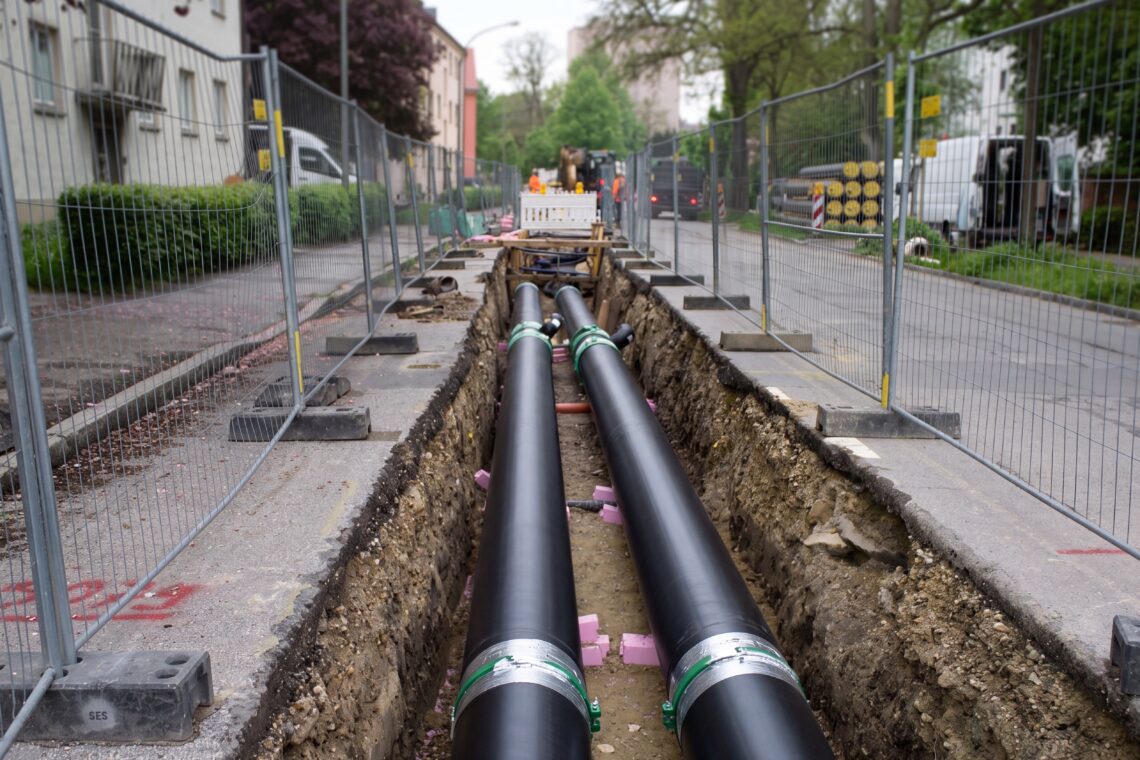 Pre-insulated district heating supply and return pipes being laid in an open trench along a European residential street — the low-temperature heat network whose per-branch flow balance keeps return temperature low