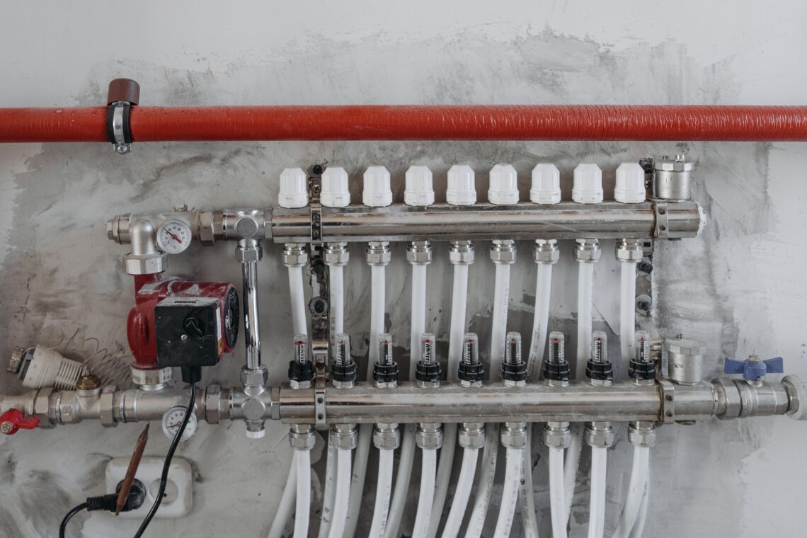 A hydronic heating manifold: one circulator pump feeding ten parallel branch circuits, each with its own flow setter — the point where surplus pump pressure becomes surplus flow.